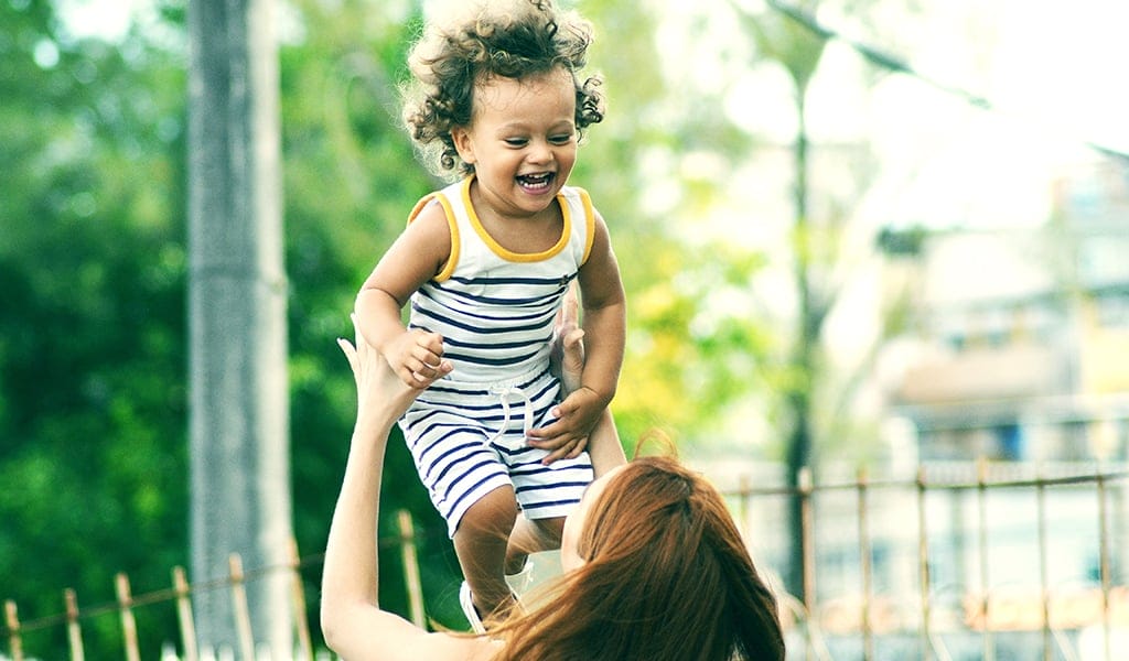 back of young woman lifting up laughing toddler